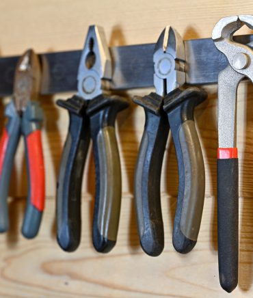 various sorts of pliers hanging on magnet hanger in workshop