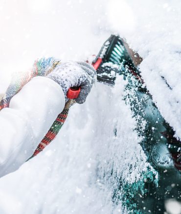 Woman cleaning snow from windshield, Scraping frozen ice glass. Winter car clean front windows.