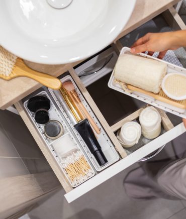 Top view of woman hands neatly organizing bathroom amenities and toiletries in drawer or cupboard in bathroom. Concept of tidying up a bathroom storage by using Marie Kondo's method.