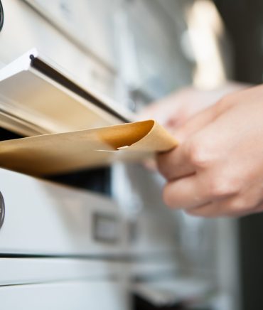 Close-up of woman's hand holding envelope and inserting in mailbox