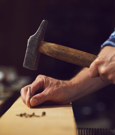 Carpenter hammering a nail into wooden plank in a carpentry shop